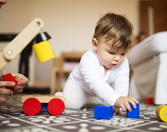 Cute little baby girl playing with her mother on a carpet in a living room.