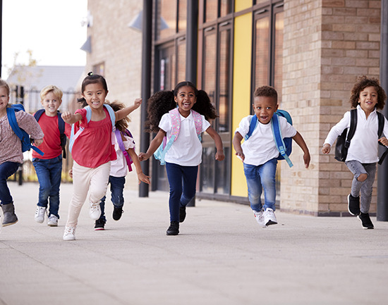 A group of smiling multi-ethnic school kids running in a walkway outside their infant school building after a lesson